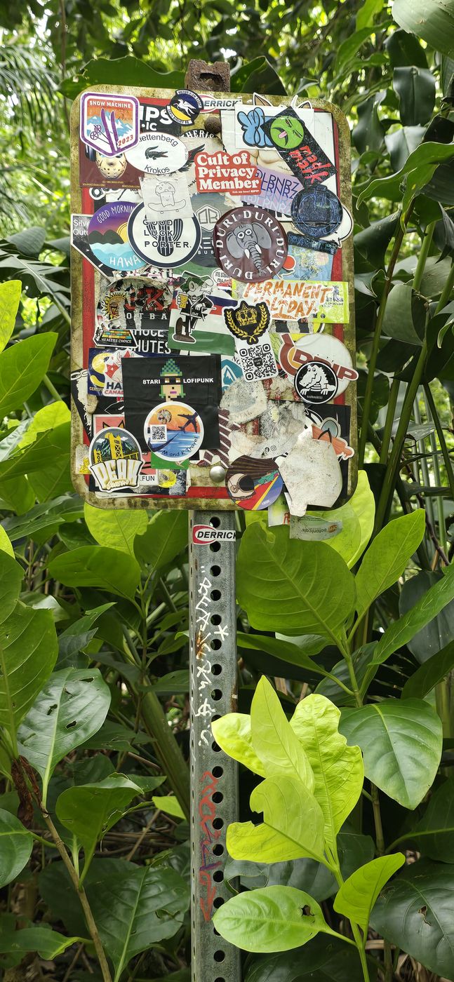 M and K Travel sticker on a sticker-covered trailhead sign in the jungle